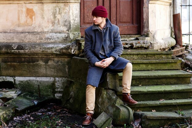 Man in grey coat and beige trousers sits on stone footsteps 