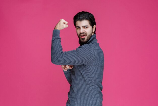 Man in grey sweater demonstrating his arm muscles.