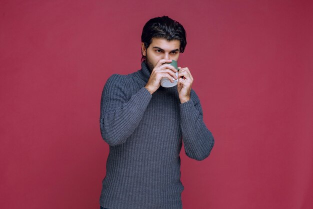 Man in grey sweater drinking coffee from the mug.