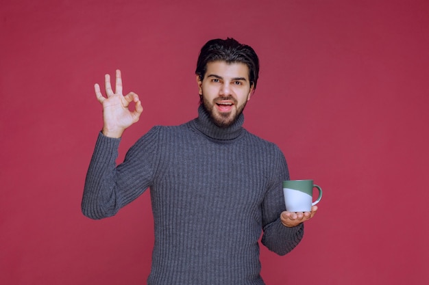 Man in grey sweater holding a coffee mug and enjoying the taste.