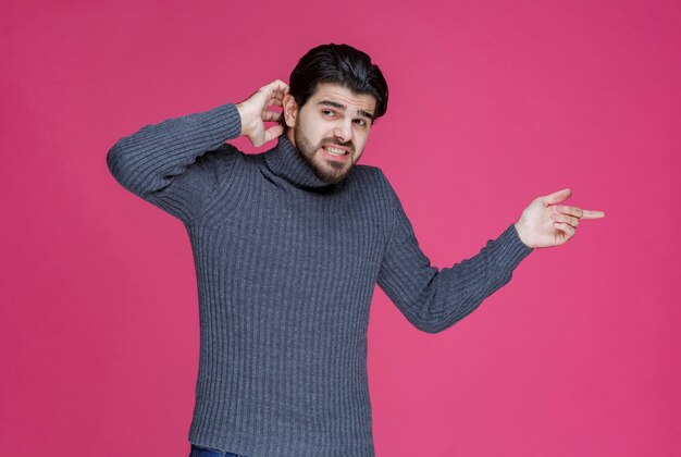 Man in grey sweater holding his ear as he has trouble with listening.