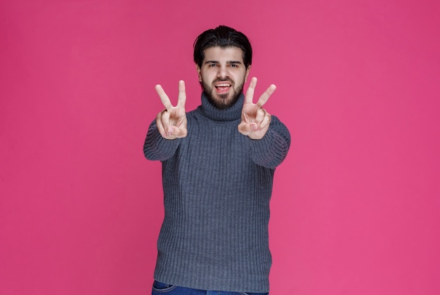 Free photo man in grey sweater making peace hand sign.