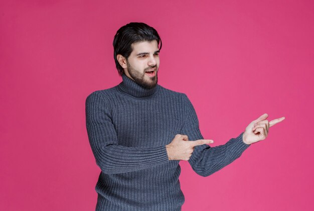 人差し指を使って何かを指さしたり、誰かを紹介したりする灰色のセーターを着た男。