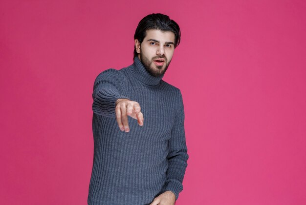 Man in grey sweater at pointing something or introducing someone using point finger.