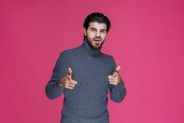 회색 스웨터를 입은 남자가 무언가를 가리 키거나 포인트 손가락을 사용하여 누군가를 소개합니다.