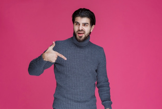 Man in grey sweater at pointing something or introducing someone using point finger.