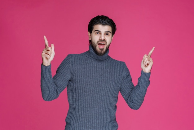 회색 스웨터를 입은 남자가 무언가를 가리 키거나 포인트 손가락을 사용하여 누군가를 소개합니다.