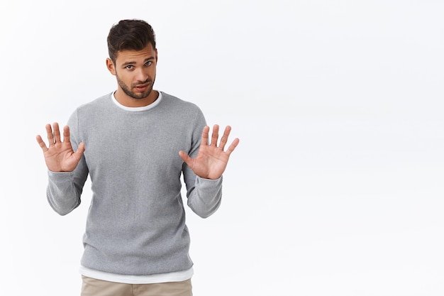 Мужчина в сером свитере поднимает руки, чтобы что-то остановить
