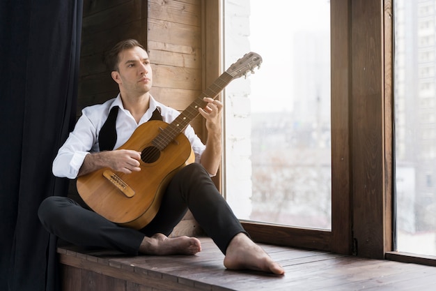 Man and guitar alongside windows