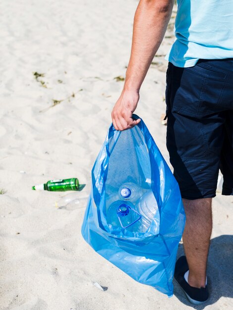 Man hand carrying blue garbage bag of waste plastic on sand