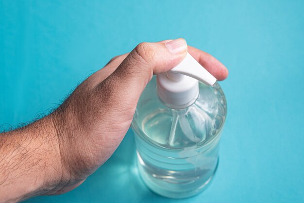 Man hand in container with alcohol gel on the light blue