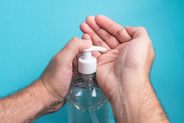 Equipaggi la mano in contenitore con il gel dell'alcool sull'azzurro