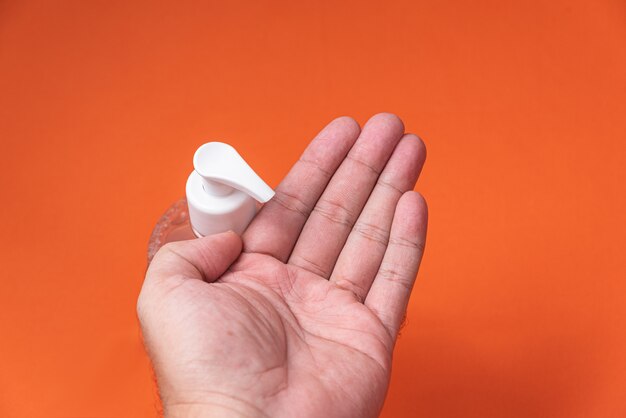 Man hand in container with alcohol gel on the orange wall