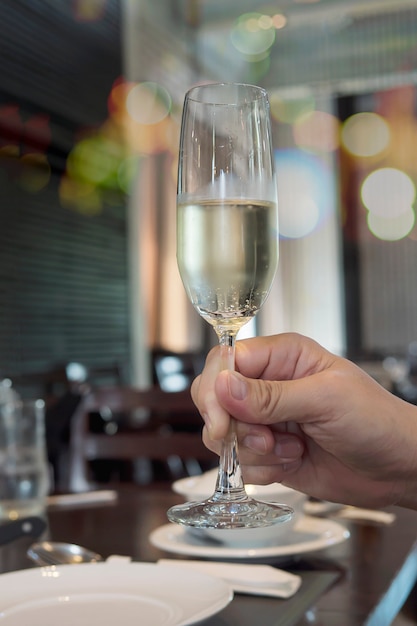 man hand holding champagne glass ready to drink over blur bokeh restaurant 