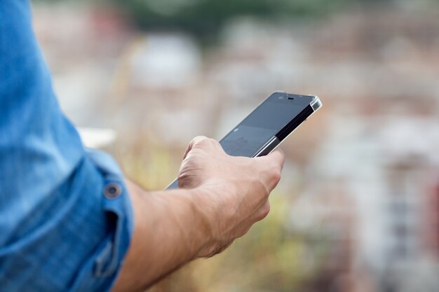 Man hand holding mobile phone in the city.