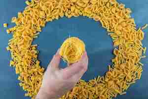 Free photo man hand holding uncooked nest noodles on a dark-blue background .