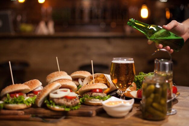 Man hand pours larger beer in a glass standing on a vintage table .Blurred counter bar . Jar of pickles.