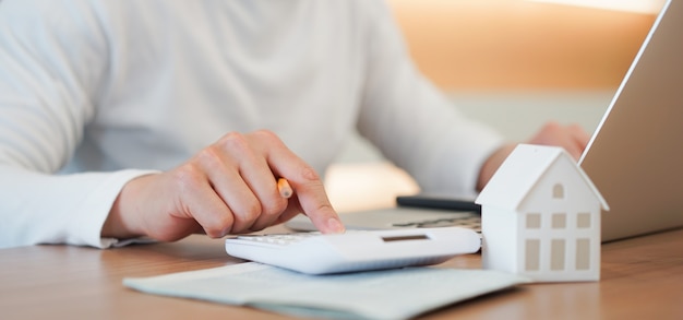 Рука человека нажмите на калькулятор, чтобы проверить и суммировать расходы по ипотечному кредиту для плана рефинансирования