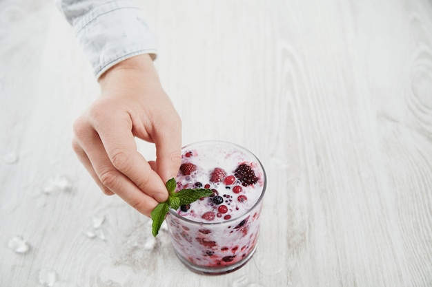 Man hand put mint leave on top of glass with milky shake cocktail with frozen berries