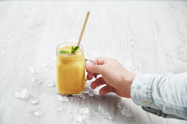 Man hand takes transparent rustic jar with tasty healthly freshly made yellow smoothie from mango