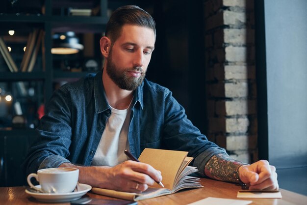 Man hand with pen writing on notebook on a wooden table. Man working at coffee shop