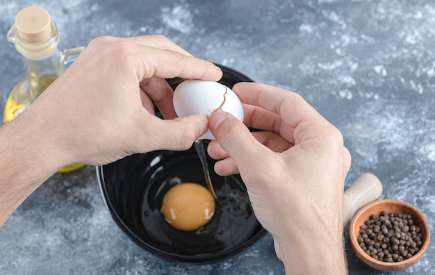 Man hands breaking eggs in bowl over grey table.