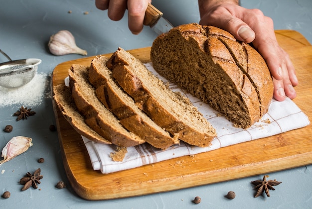 Мужские руки режут ножом кусок ржаного хлеба