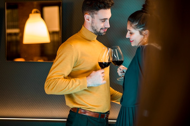Мужчина и счастливая женщина звенят бокалами вина в комнате