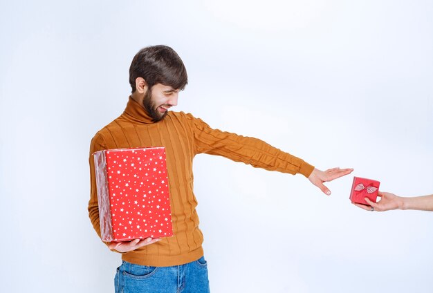 Мужчина держит большую красную подарочную коробку и хочет взять еще одну маленькую.