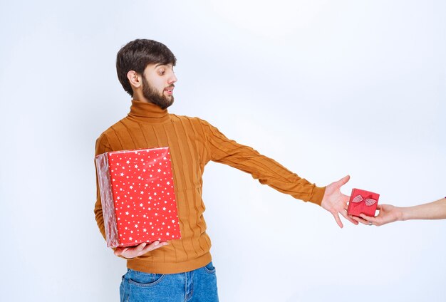 Man has a big red gift box and longing hand to take another small one.