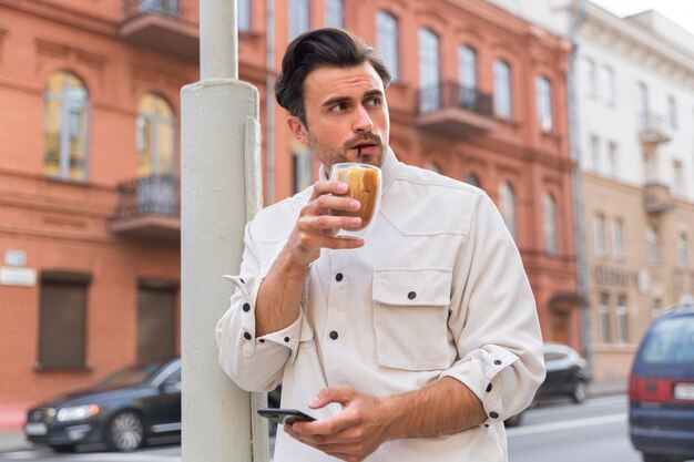 Мужчина делает перерыв на кофе со льдом, используя смартфон на улице