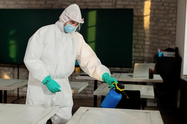 Мужчина в защитном костюме дезинфицирует класс из-за пандемии коронавируса