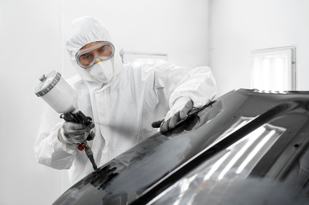 Man in hazmat suit using gun to paint car in the shop