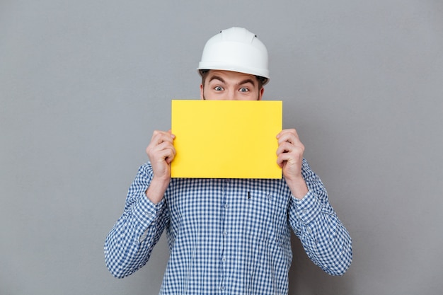 Free photo man in helmet hiding behind the blank board