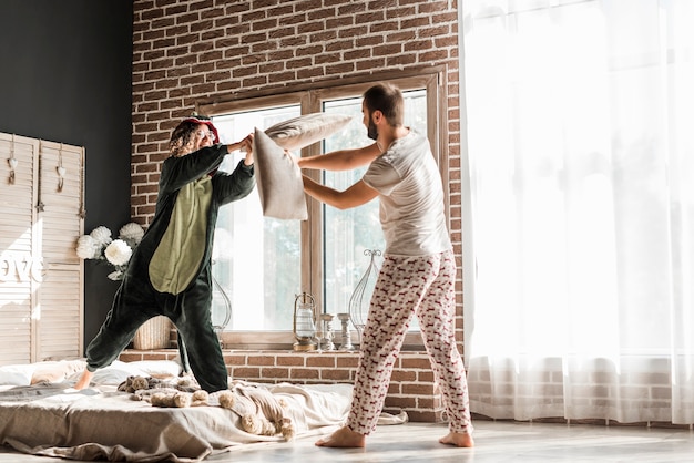 Man and her girlfriend in costume having funny pillow fight at home