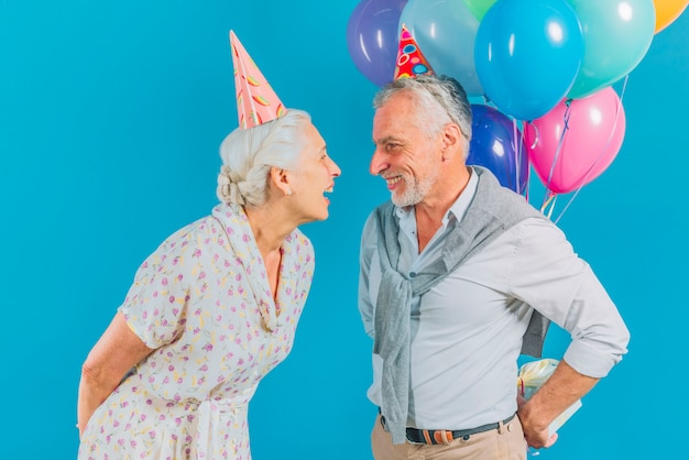 青い背景で彼の妻から誕生日プレゼントを隠している男