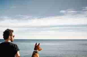 Free photo man and his dog on the beach admiring the sea