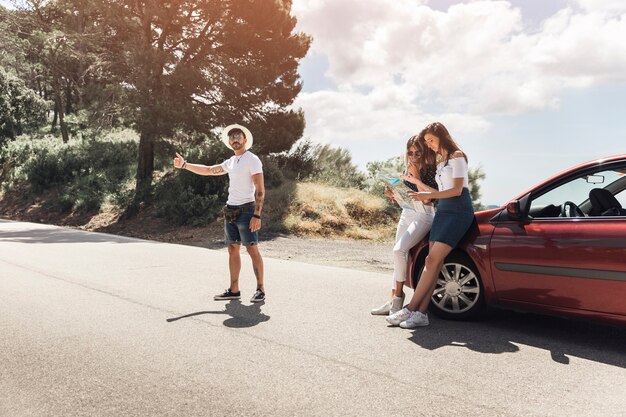 Man hitchhiking on road and her friends looking at map
