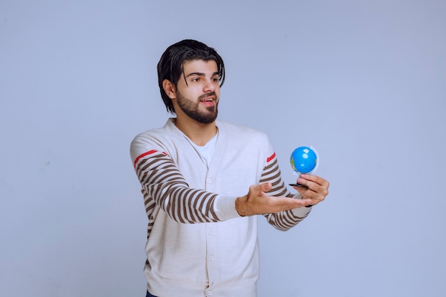 Бесплатное фото Мужчина держит мини-глобус, трясет им и пытается угадать местоположение.
