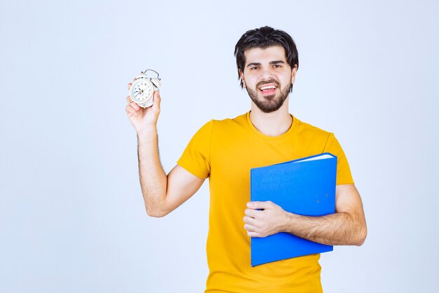 Man holding an alarm clock and a blue folder.