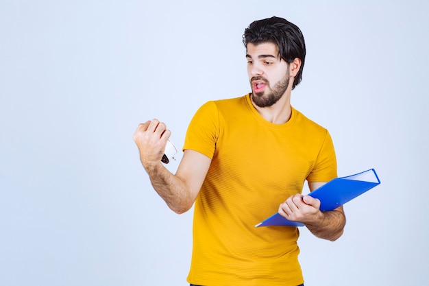 Man holding an alarm clock and a blue folder.