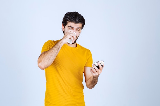 Man holding an alarm clock and drinking coffee.