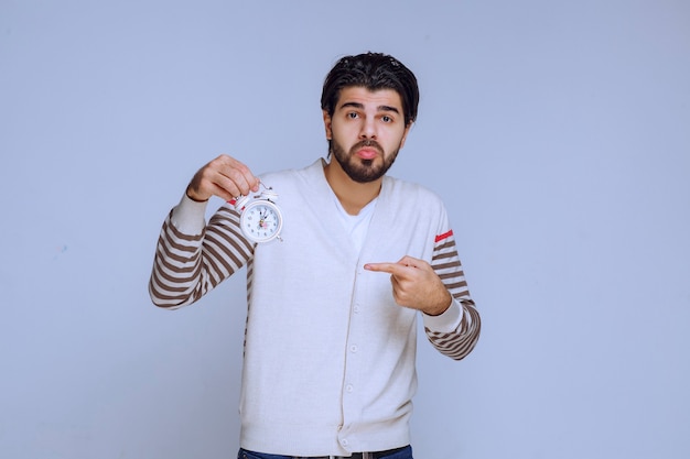 Man holding an alarm clock and looks confused