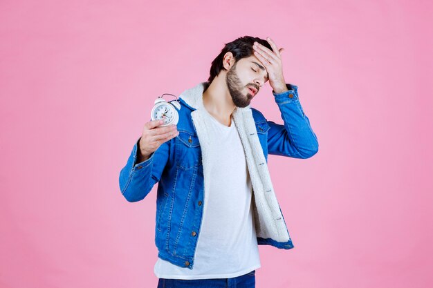 Man holding an alarm clock and looks still sleepy