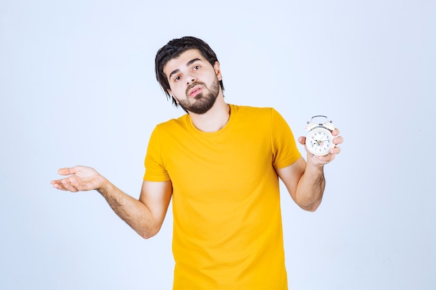 Man holding an alarm clock and looks tired.