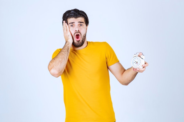 Man holding an alarm clock and noticed that he is late.