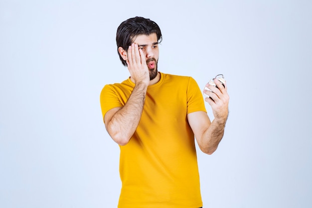 Free photo man holding an alarm clock and noticed that he is late.