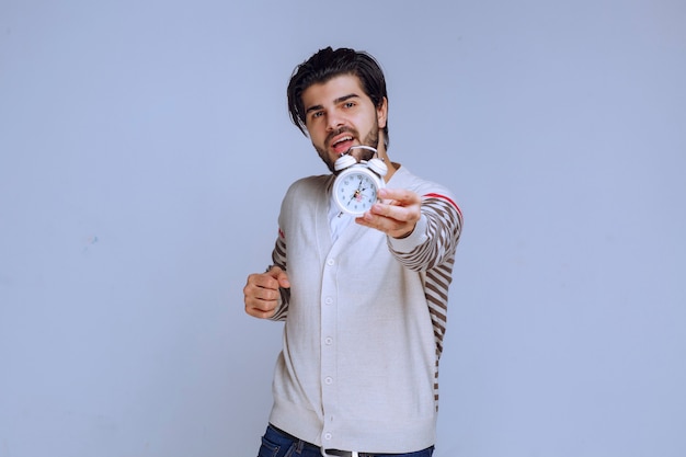 Free photo man holding an alarm clock and offering it to the customer.