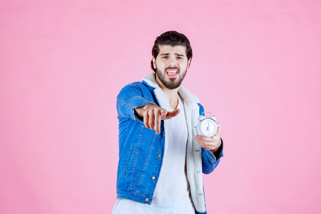 Man holding an alarm clock and pointing ahead