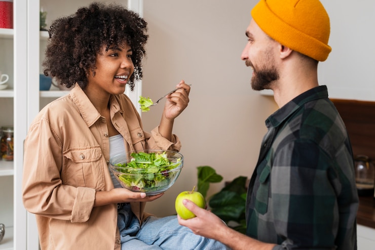 Free Photo man holding apple and looking at woman eating salad